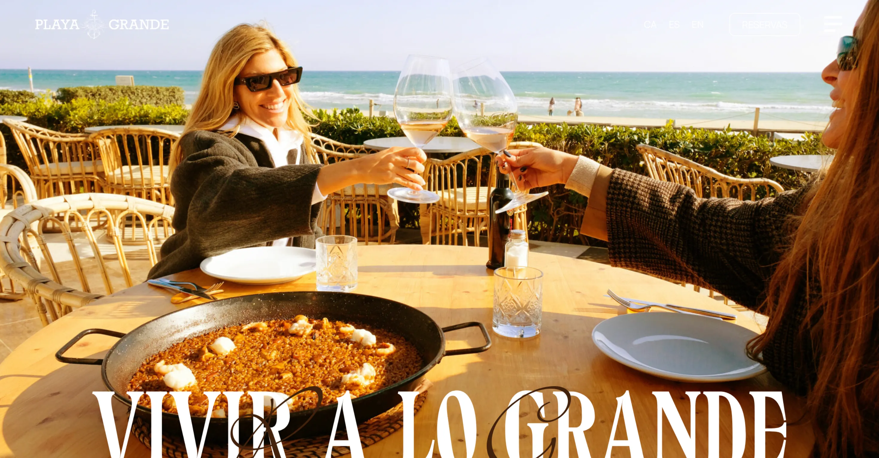 Page d'accueil du site Playa Grande : deux personnes trinquent devant une paella face à la mer, sous le titre « Vivir a lo grande ».